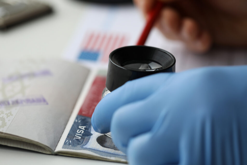 Specialist with loupe checking authenticity of american visa in passport close-up
